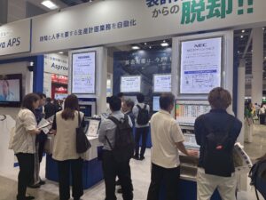 Crowd of people at a busy trade show booth with posters and screens on display walls in a bright hall