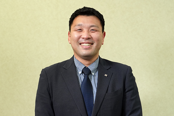Smiling man in a dark suit and blue tie posing for a professional portrait.