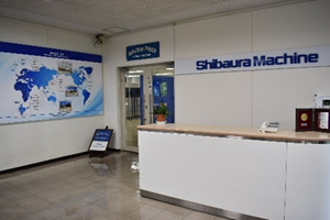 Reception area of Shibaura Machine with a white counter and a world map mural on the left wall.